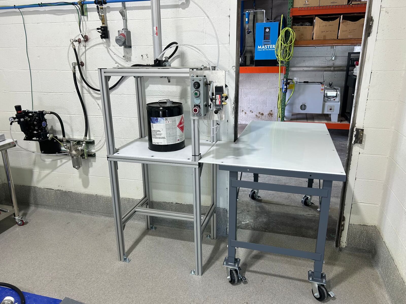 Mix room dispensing station with a pail on a stainless stand and air-driven pump on the wall